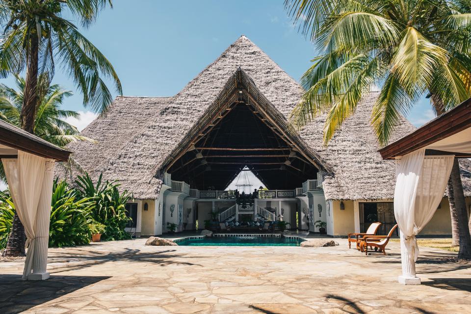 Looking into the lofty, open-air living room, from which a saltwater pool extends out to the terrace. The makuti thatched roof is composed of sun-dried coconut palm leaves hand-sewn into intricate layers.