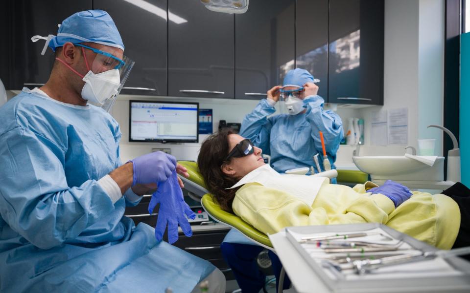 Dentist Fiez Mughal (L) and Dental Nurse Johanna Bartha (R) don their protective gloves and face shields in one of the six surgery rooms at East Village, London - Leon Neal/Getty