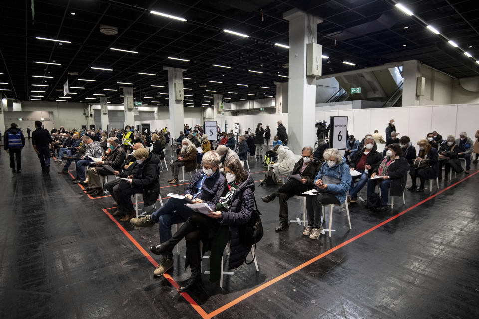 People wait with mouth-to-nose coverage in a vaccination center in Cologne, Germany, Sunday, April 4, 2021. In North Rhine-Westphalia, people aged 60 and over have been able to get vaccinated against the coronavirus with the active ingredient from Astrazeneca since this weekend. The rush for the vaccination appointments for the age group 60 plus had already led to overloaded lines on the phone and on the Internet in the early morning of Holy Saturday, 03.04.2021. (Marius Becker/dpa via AP)