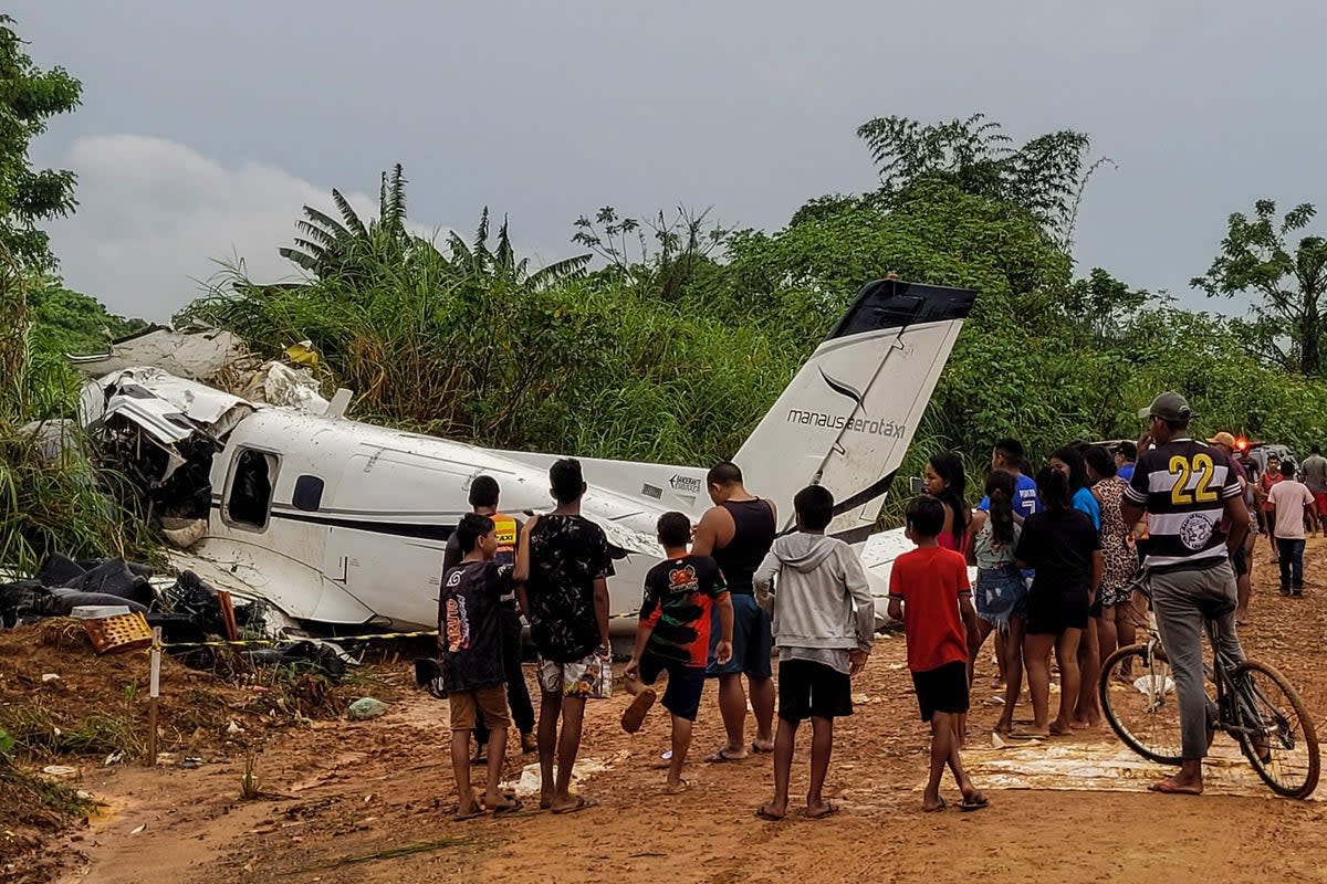 People stand looking at the site where an Embraer EMB-110 aircraft of the Manaus Aerotaxi airline crashed, causing the deaths of 14 people during the plane's landing the previous day at Barcelos airport (AFP via Getty Images)