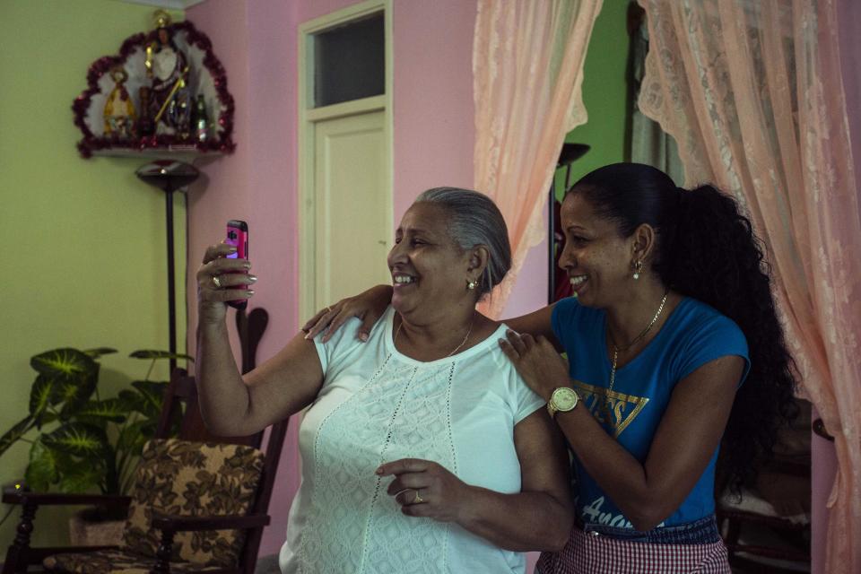 In this Jan. 6, 2017 photo Yolanda Mollinedo looks at her granddaughter Alejandra in Virginia, United States, on her smartphone using a video chat application beside her niece Yulisleidi with the new experimental internet in the living room of her home in Havana, Cuba. The home internet test program selected some 2,000 residents of Old Havana to receive free connections for two months before a planned expansion and the start of billing for the service. (AP Photo/Desmond Boylan)