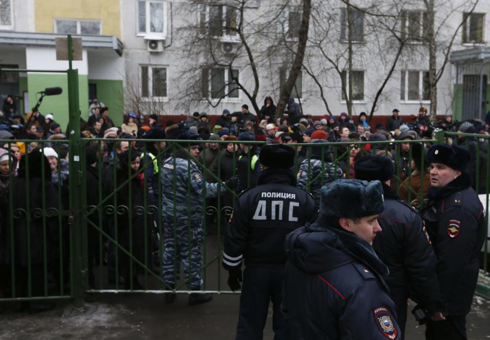 Interior Ministry members stand guard as people gather behind a fence near a high school, on the outskirts of Moscow