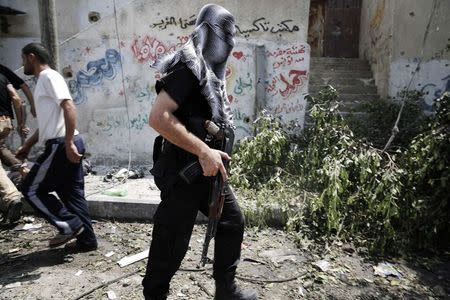 A masked Palestinian gunman moves across a rubble-strewn street in the Shejaia neighbourhood, which was heavily shelled by Israel during fighting, in Gaza City July 20, 2014. REUTERS/Finbarr O'Reilly