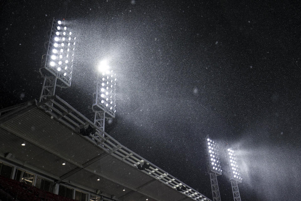 Falling snow is illuminated by stadium light during the eighth inning of a baseball game between the Arizona Diamondbacks and the Cincinnati Reds in Cincinnati, Tuesday, April 20, 2021. The game was suspended due to inclement weather. (AP Photo/Aaron Doster)