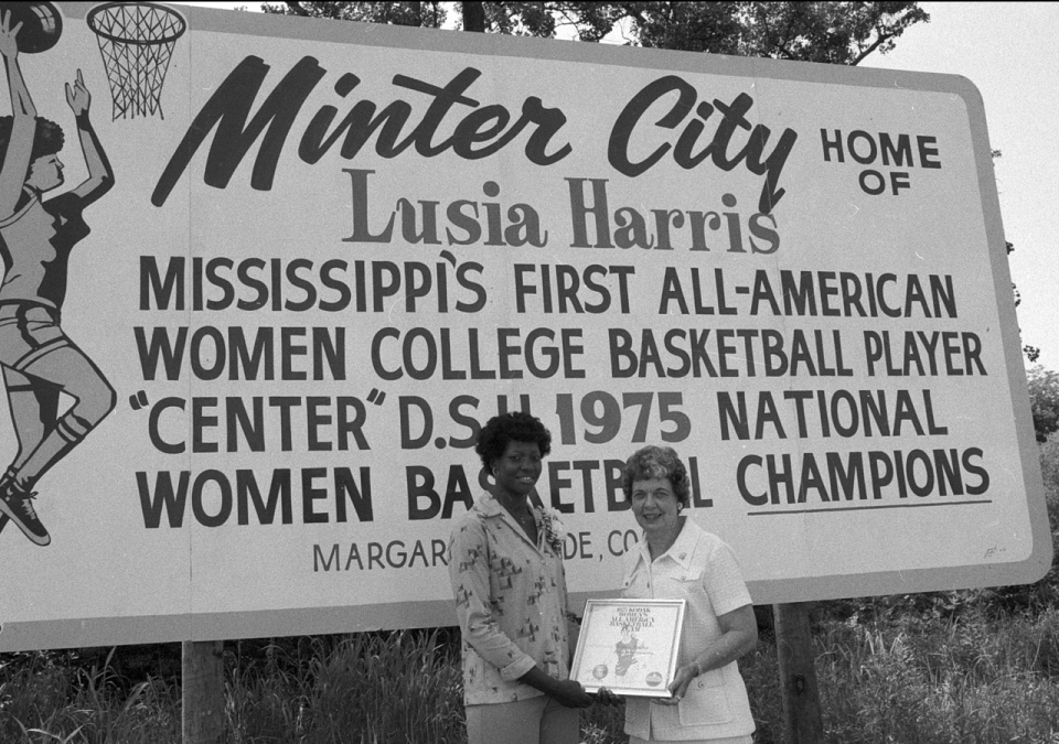 Lusia Harris stands in front of a sign honoring her as Minter City, Mississippi's, first All-American women's college basketball player.,