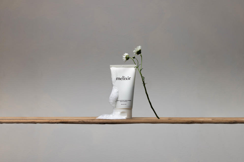 Melixir Vegan Clarifying Foam Cleanser in white packaging with foam and a white flower