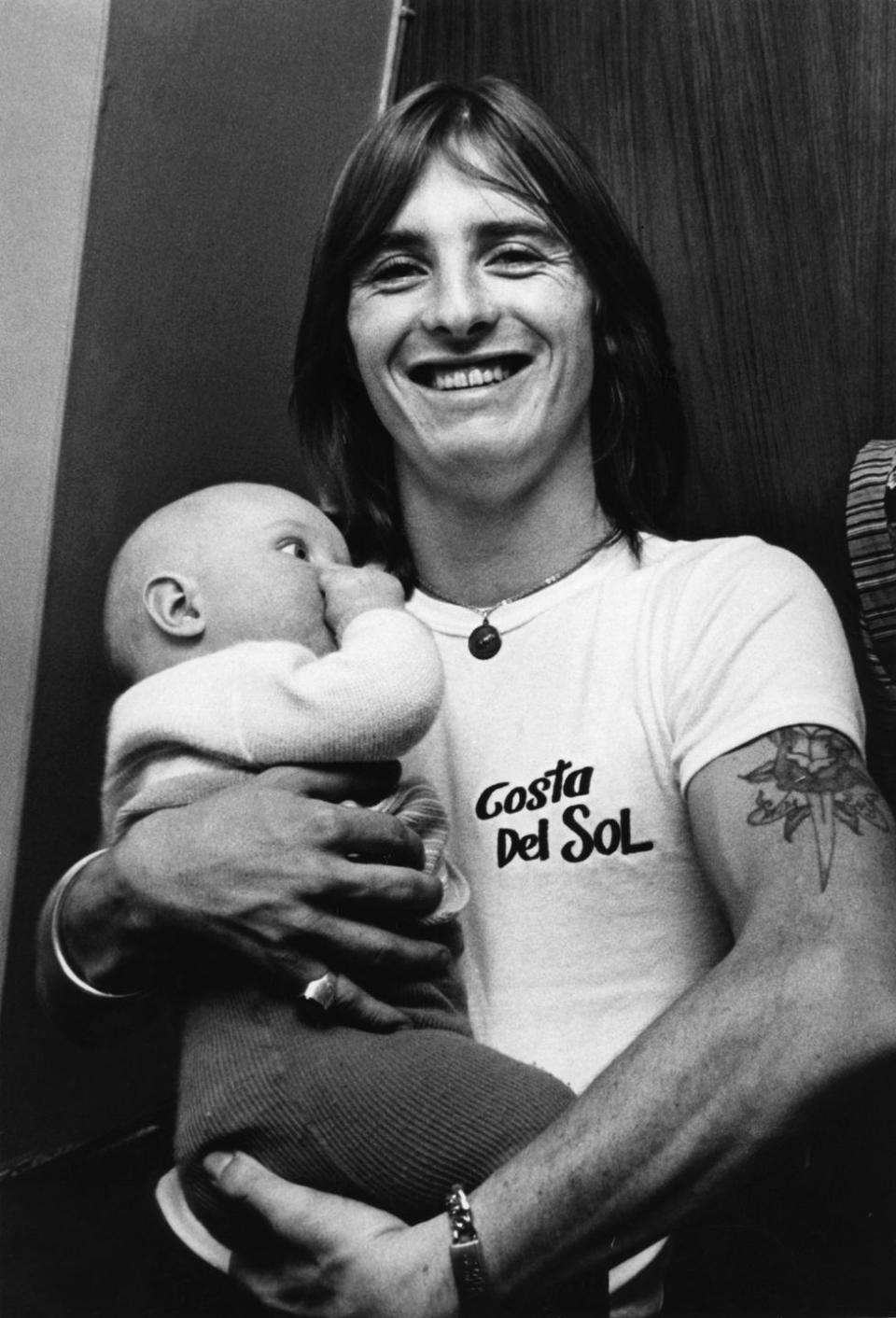 <p>AC/DC drummer, Phil Rudd, holds a baby backstage at one of their concerts. </p>