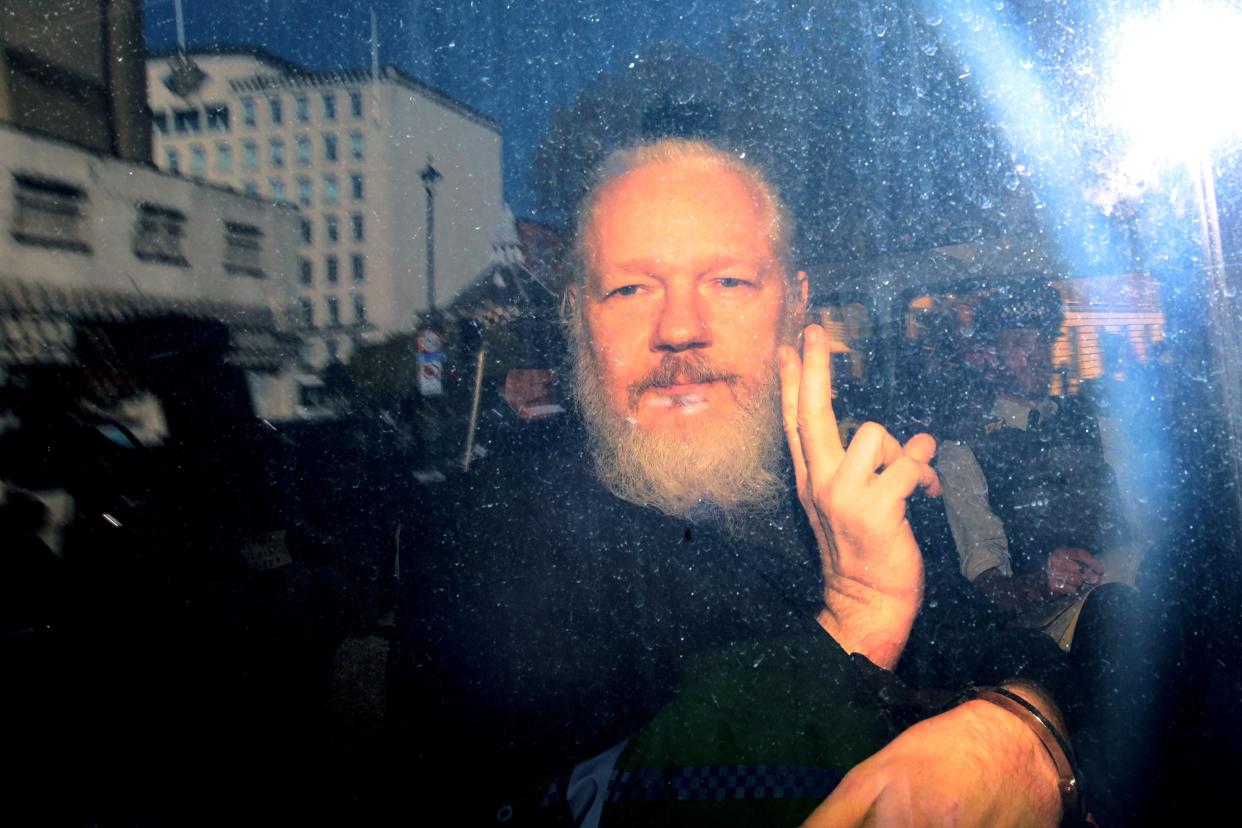 Julian Assange flashes a peace sign, handcuffs visible around his wrists, to the media from a police vehicle during his arrival at Westminster Magistrates court on April 11, 2019 in London, England.  After weeks of speculation, the Wikileaks founder was arrested by Scotland Yard Police Officers inside the Ecuadorian Embassy in Central London on Thursday morning.