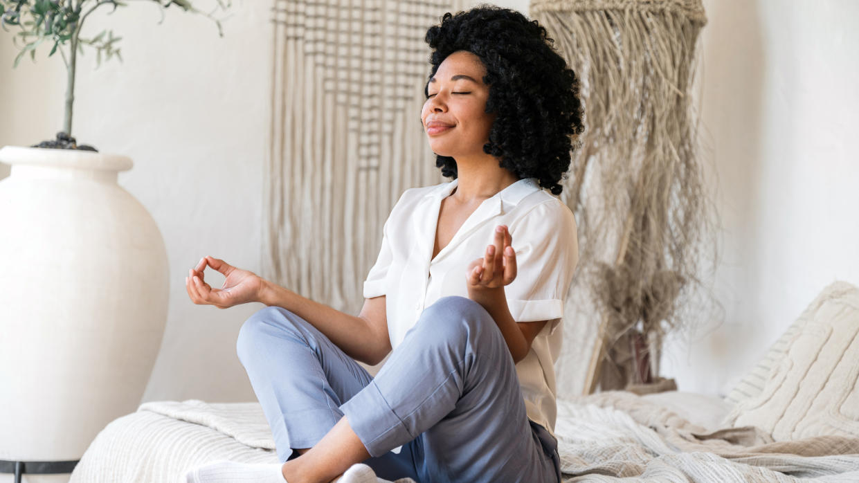  Woman doing peaceful meditative yoga pose on bed first thing in the morning. 