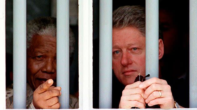 US President Bill Clinton and South African President Nelson Mandela peer through the bars of the cell in which Mandela spent 17 years while incarcerated by the former South African government, on Robben Island. Photo: Getty.