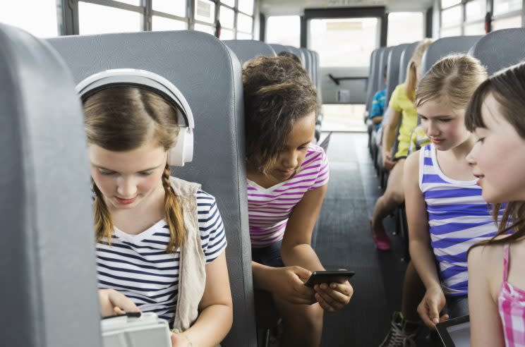 Schoolgirls using smart devices on school bus (Getty)