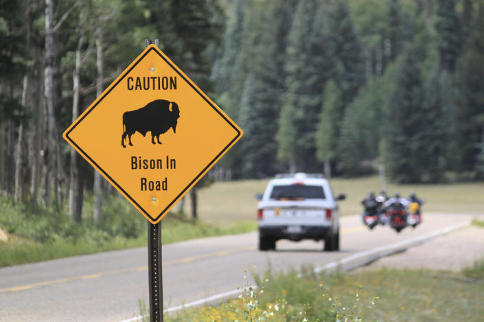 FILE - In this July 31, 2016 photo, a park ranger and a group of motorcyclists pass a sign warning of bison within the Grand Canyon National Park in northern Arizona. Grand Canyon National Park has decided not to extend a pilot project this fall 2022 that used volunteers to kill bison to downsize the herd. New surveys show the herd roaming the far reaches of northern Arizona is closer to the goal of about 200. (AP Photo/Susan Montoya Bryan, File)