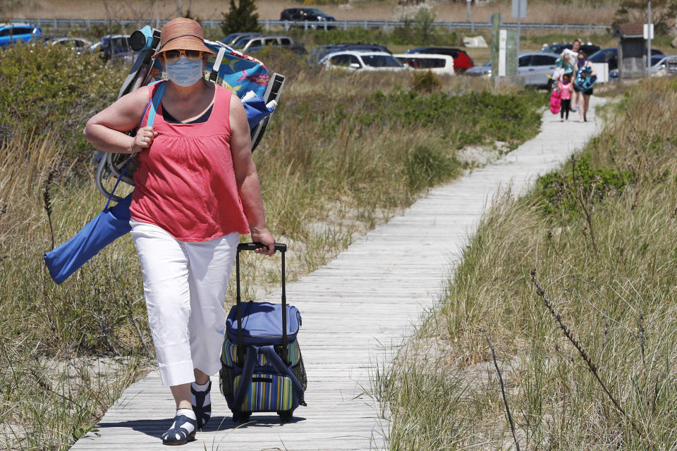 Jody Curran wears a protective mask due to the COVID-19 virus outbreak as she walks on a one way pathway towards Good Harbor Beach in Gloucester, Mass., Friday, May 22, 2020. Beaches in Gloucester reopened with restrictions on Friday after being closed two months ago due to the pandemic. (AP Photo/Charles Krupa)