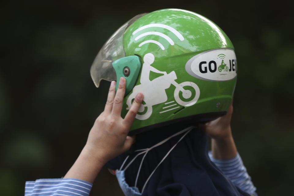 A woman holds a Gojek helmet after arriving at a station in Jakarta, Indonesia, Monday, May 17, 2021. Indonesian ride hailing company Gojek and e-commerce firm Tokopedia said Monday that they are merging, in the largest ever deal in the country's history. (AP Photo/Achmad Ibrahim)