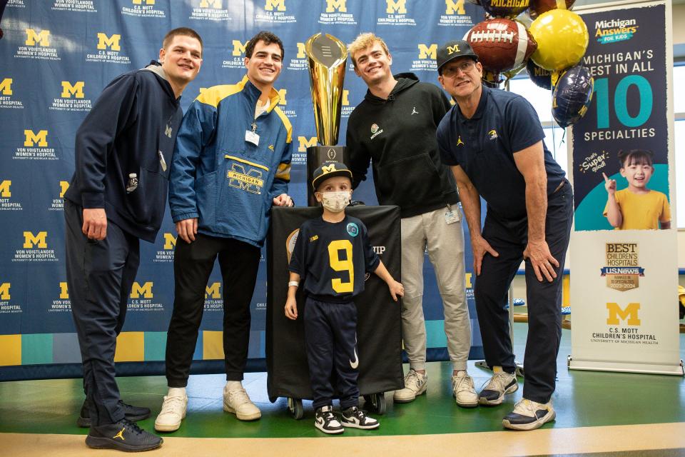From left, Michigan defensive back Jesse Madden, wide receiver Jake Thaw, quarterback Davis Warren, and head coach Jim Harbaugh have their photo taken with Nicholas Rinehart, 6, next to the national championship trophy at C.S. Mott Children's Hospital in Ann Arbor on Friday, Jan. 12, 2024.