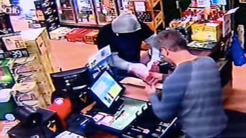 The cashier hands over money after having a gun pointed at him. Photo: CCTV