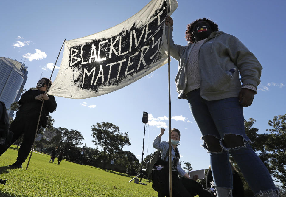 A couple hold a banner as thousands gather at a rally supporting the Black Lives Matter and Black Deaths in Custody movements in Sydney, Sunday, July 5, 2020. (AP Photo/Rick Rycroft)