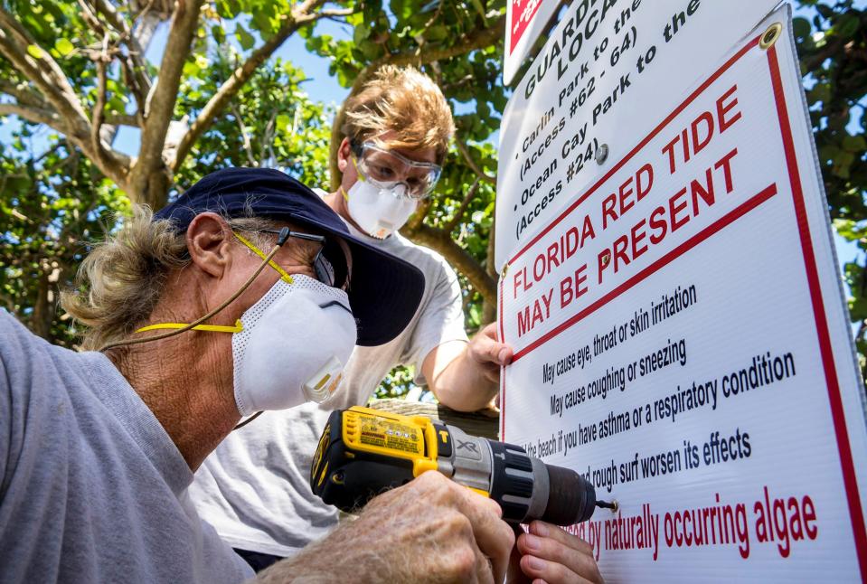 In October 2018, Palm Beach County ocean rescue Captain Rick Welch, left, and lifeguard Russ Gehweiler, right, install newly printed signs warning visitors of the red tide outbreak along A1A, south of Indiantown Road in Jupiter.  (Richard Graulich / The Palm Beach Post)