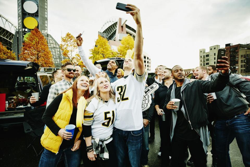group of friends taking selfies in stadium parking lot before football game