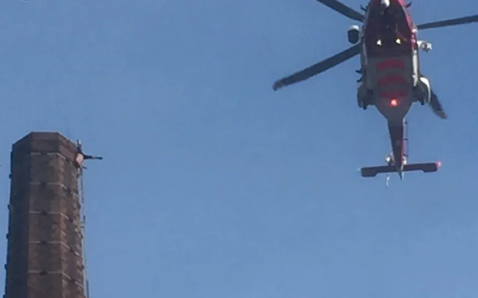 The man is seen here, in an image from social media, dangling from the top of the former mill chimney (Twitter EMURRIE91)