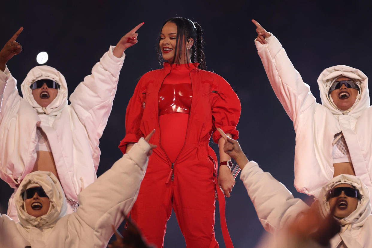 Rihanna onstage wearing an all-red outfit, amid dancers wearing all-white outfits and sunglasses.