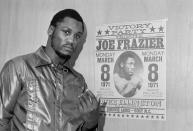 FILE - Heavyweight champ Joe Frazier poses by a poster advertising his "victory party" as he leaves his dressing room after a final public workout in Philadelphia ahead of his title defense fight against Muhammad Ali in New York on March 8, in this March 6, 1971, file photo. Their first fight at Madison Square Garden was so epic it was billed as the Fight of the Century, and 50 years later it reigns undefeated. (AP Photo/Bill Ingraham, File)