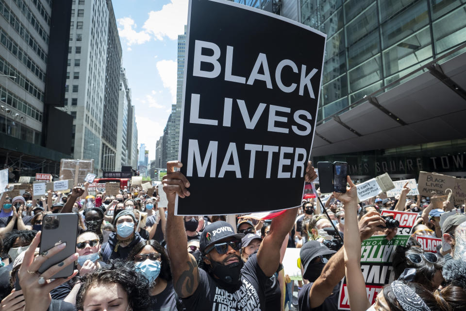 MANHATTAN, NY - JUNE 07:  An African American protester wearing a mask around his neck and a hat that has Black Power in Times Square holds up a large sign that reads, "Black Lives Matter" with thousands of people behind him.  This was part of the Black Lives Matter New York (BLMNY) protest that offered a Blueprint for change and called on New York state legislators and members of Congress to end the slaughter of Black persons by the very institutions charged with protecting them.  The Blueprint is a policy platform to reform failed statutes and regulations and to  begin reforming to a more civil and just society. This includes the I Can't Breathe Act, the Blue Wall Act, repealing of 50-A statute and includes housing and education reforms. Protesters keep taking to the streets across America and around the world after the killing of George Floyd at the hands of a white police officer Derek Chauvin that was kneeling on his neck during his arrest as he pleaded that he couldn't breathe. The protest are attempting to give a voice to the need for human rights for African American's and to stop police brutality against people of color.  Many people were wearing masks and observing social distancing due to the coronavirus pandemic.  Photographed in the Manhattan Borough of New York on June 07, 2020, USA.  (Photo by Ira L. Black/Corbis via Getty Images)