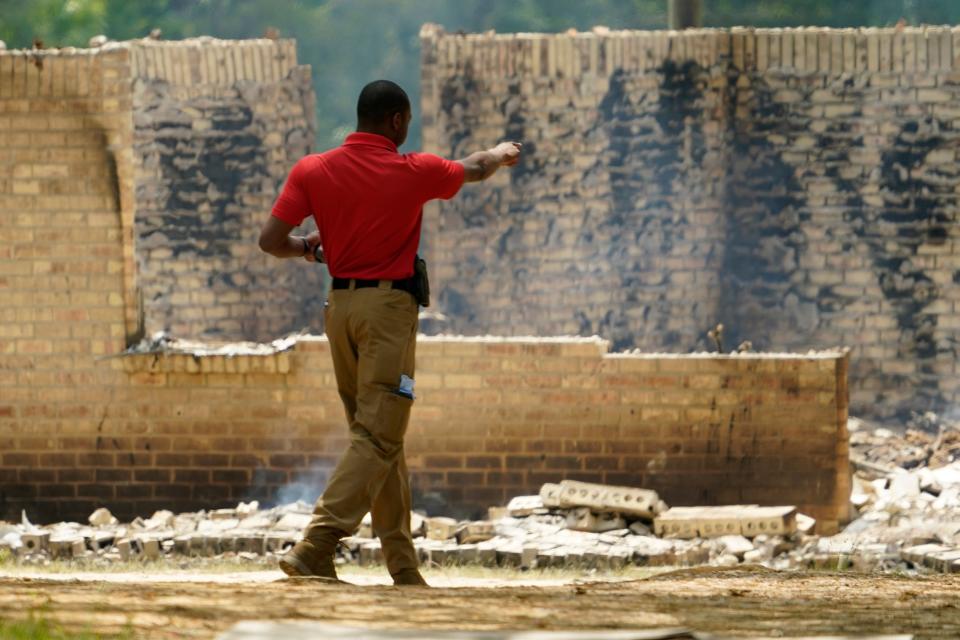 An investigator gestures at the remnants of a burned out house where authorities believe a man who escaped from a Mississippi jail over the weekend with three others, and is suspected of killing a pastor, is believed to be dead after a shootout with authorities and barricaded himself inside a burning home near Conway, Mississippi, Wednesday morning, April 26, 2023 (AP)