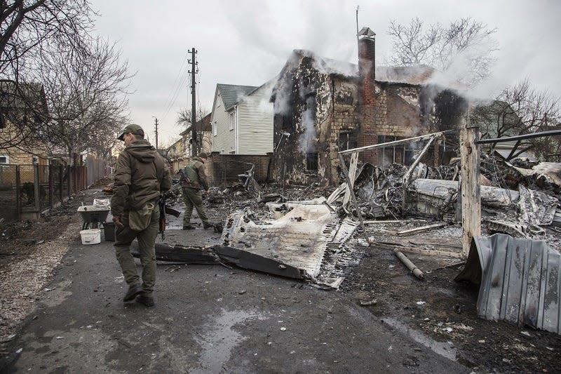 Ukrainian servicemen walk at fragments of a downed aircraft seen in in Kyiv, Ukraine, Friday, Feb. 25, 2022. It was unclear what aicraft crashed and what brought it down amid the Russian invasion in Ukraine Russia is pressing its invasion of Ukraine to the outskirts of the capital after unleashing airstrikes on cities and military bases and sending in troops and tanks from three sides.