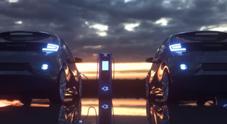 Two electric vehicles facing a dark sky, sunset background with one EV hooked up to an EV charger in between the two cars