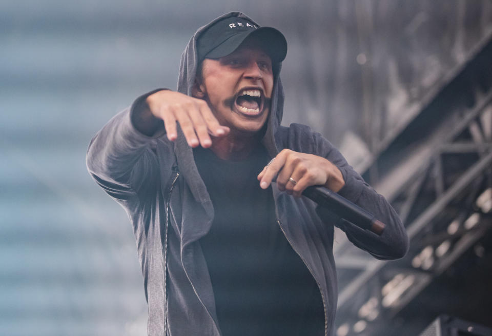 NF perfoms on stage with black paint markings around his mouth while holding a microphone in his hand.