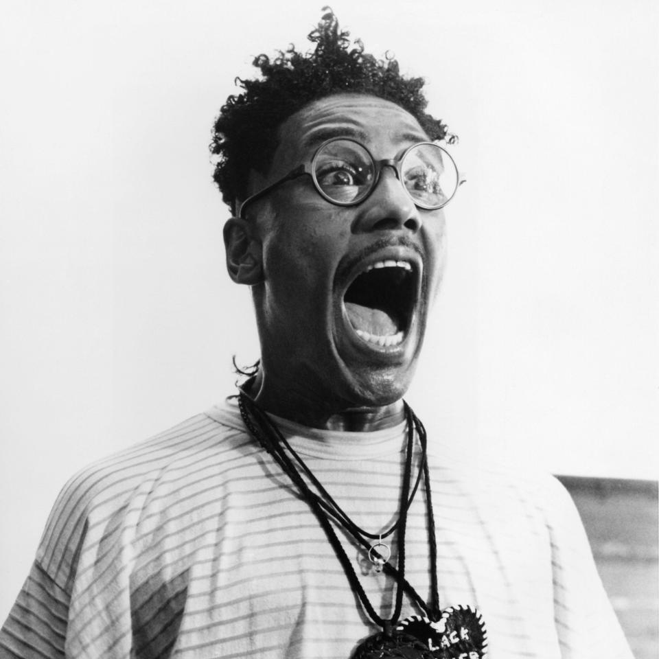 Person with expressive face wearing glasses, striped shirt, and 'Black Power' necklace