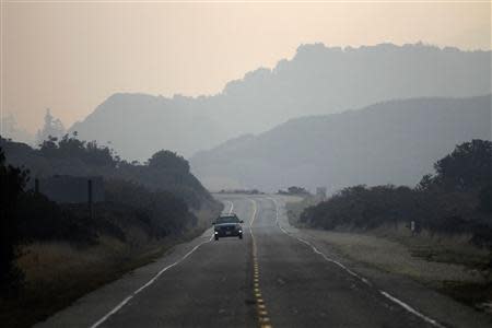 A car drives north on Highway 1 through smoke caused by the Pfeiffer fire in Big Sur, California, December 18, 2013. Hundreds of firefighters battled to gain control of a raging wildfire along central California's scenic Big Sur coastline on Tuesday, hampered by steep and brushy terrain and narrow roads, officials said. REUTERS/Michael Fiala