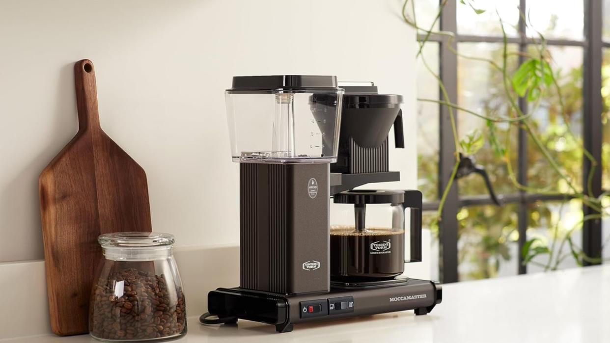  The Moccamaster KGBV Select on a countertop with a wooden board and coffee canister beside it. 