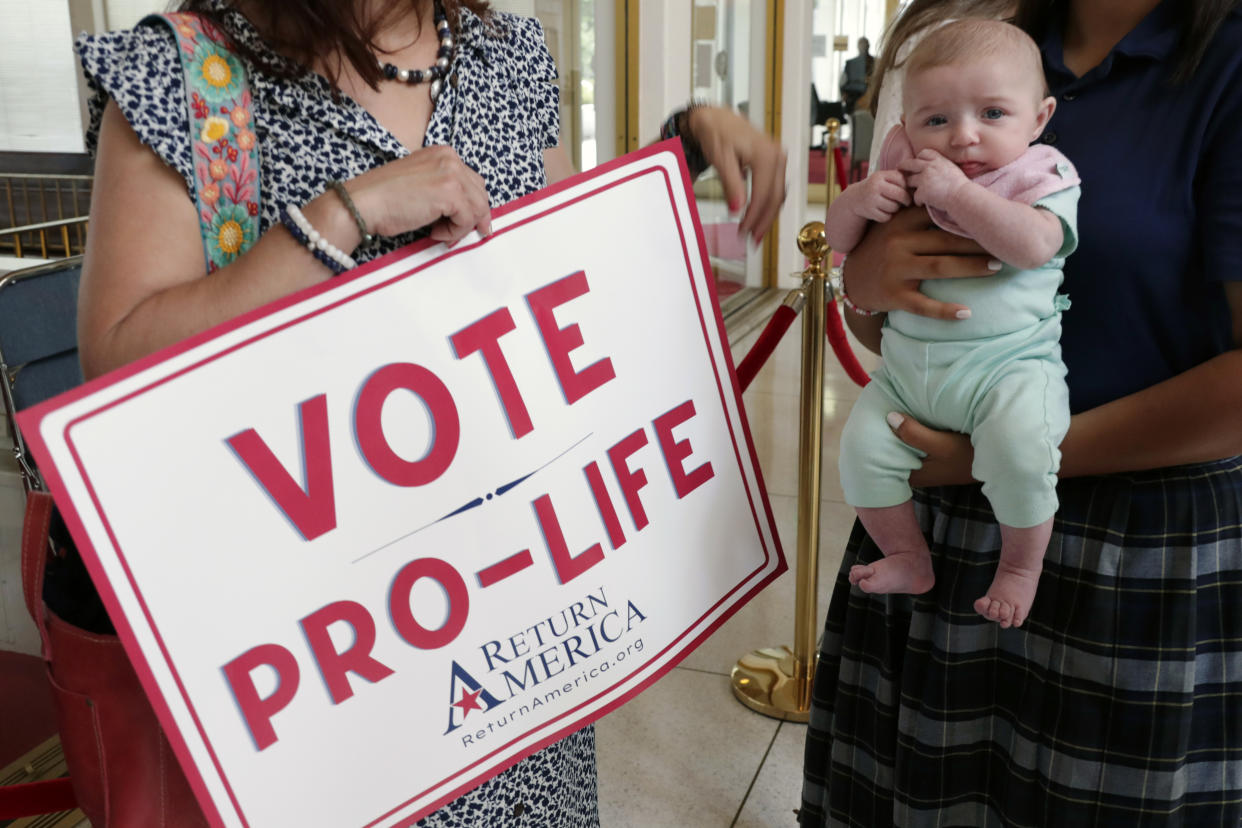 An anti-abortion supporter from Moore County holds a sign next to a 3-month-old baby as they wait to enter the Senate gallery, Tuesday, May 16, 2023, in Raleigh, N.C., as state legislators debate on whether to override Democratic Gov. Roy Cooper's veto of a bill that would change the state's ban on nearly all abortions from those after 20 weeks of pregnancy to those after 12 weeks of pregnancy. Both the Senate and House had to complete successful override votes for the measure to be enacted into law. (AP Photo/Chris Seward)