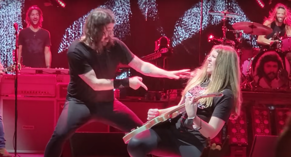 A young fan playing guitar on stage alongside Dave Grohl at a live show.