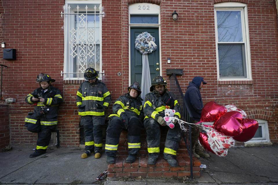 A Baltimore firefighter holds balloons given to him by neighbor Darlene Cucina as a group of fire officials sit on a stoop across the street where several firefighters died in a building collapse while battling a two-alarm blaze in a vacant row home, Monday, Jan. 24, 2022, in Baltimore. (AP Photo/Julio Cortez)