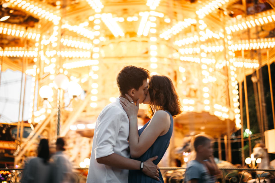 A couple kisses passionately in front of a lit-up carousel