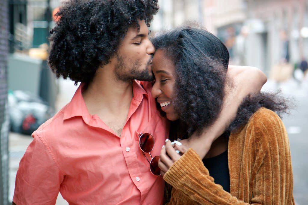 A man kisses his significant other on the head as they walk downtown. 