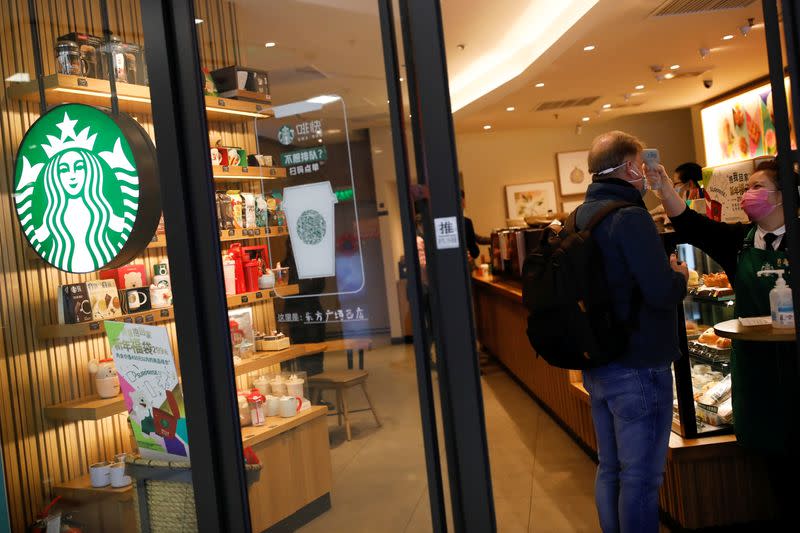 Worker uses a thermometer to check the temperature of a customer as he enters a Starbucks shop as the country is hit by an outbreak of the new coronavirus, in Beijing