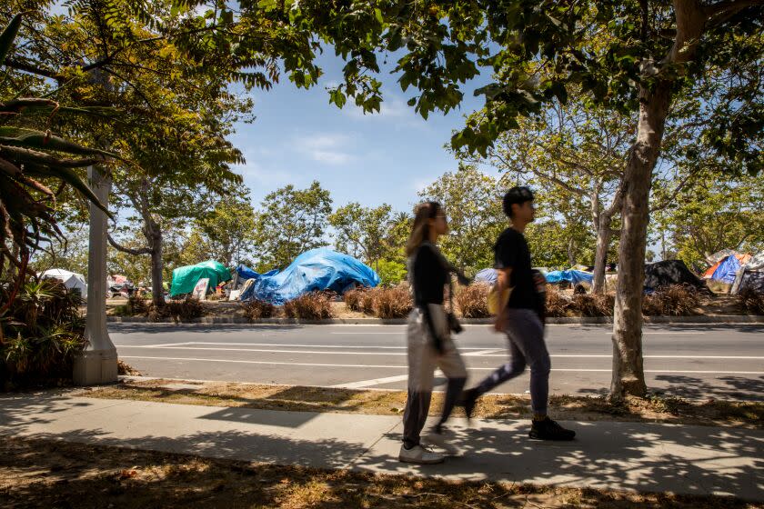 Venice, CA - May 26: People walk along S. Venice Boulevard, with tents and various structures seen behind them, in Centennial Park in Venice, CA, Thursday, May 26, 2022. The homeless encampment is at the center of the CD 11 race, being run by candidates Traci Park, Greg Good, Erin Darling, Mike Newhouse, Allison Holdorff Polhill, Jim Murez, Mat Smith. (Jay L. Clendenin / Los Angeles Times)