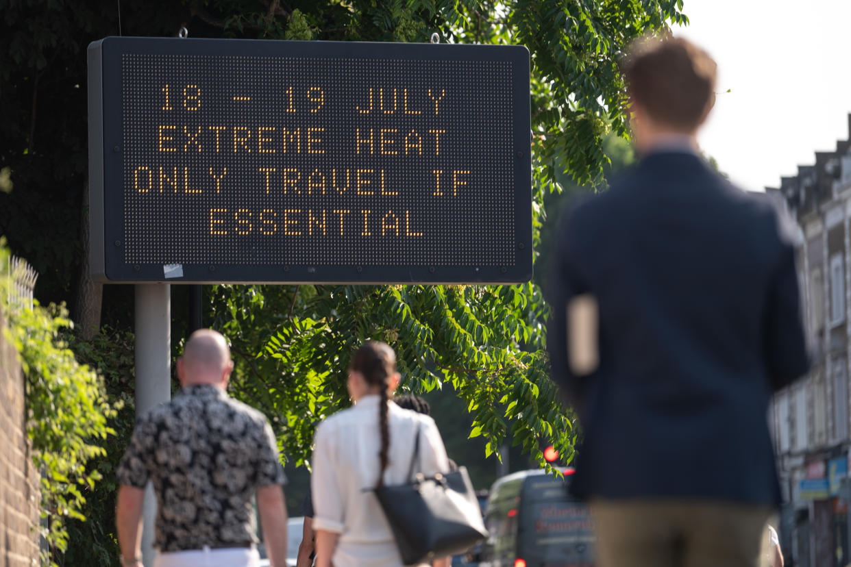 Passersby walk by a sign that reads: 18-19 July, extreme heat, only travel if essential. 