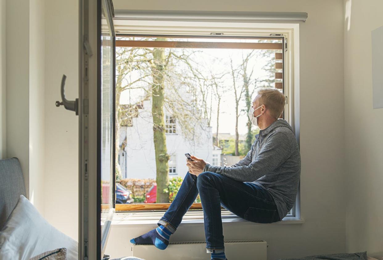 <span class="caption">Open windows are the simplest way to increase air flow in a room.</span> <span class="attribution"><a class="link " href="https://www.gettyimages.com/detail/photo/man-with-mask-looking-out-of-window-royalty-free-image/1215148858?adppopup=true" rel="nofollow noopener" target="_blank" data-ylk="slk:Justin Paget / Digital Vision via Getty Images;elm:context_link;itc:0;sec:content-canvas"> Justin Paget / Digital Vision via Getty Images</a></span>