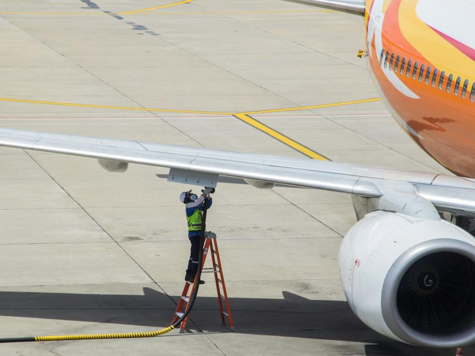 An airline worker looks up at the wing of an aircraft.