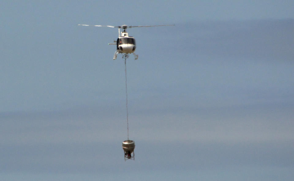 In this Nov. 11, 2012 photo released by Galapagos National Park, a helicopter tests carrying a container that will hold poisonous bait to kill rats on the Galapagos Islands, over Baltra Island. To preserve the unique birds, reptiles and native plants that make the Galapagos Islands such an ecological treasure, authorities will start on Wednesday, Nov. 14, 2012 phase II of a mass kill-off of black and Norway rats, an invasive species introduced to the Pacific Ocean islands by whalers and buccaneers beginning in the 17 century. (AP Photo/Galapagos National Park)