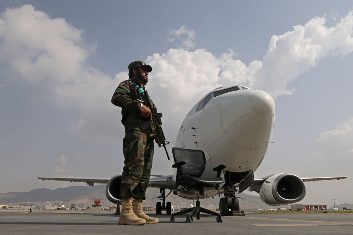 A Taliban fighter stands guard next to an Ariana Afghan Airlines aircraft on the tarmac at the airport in Kabul  (AFP via Getty Images)