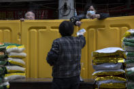 A vendor wearing a protective mask against the coronavirus returns change to a customer over a barrier used to seal off a neighborhood in Wuhan, China, Friday, April 3, 2020. Sidewalk vendors wearing face masks and gloves sold pork, tomatoes, carrots and other vegetables to shoppers Friday in the Chinese city where the coronavirus pandemic began as workers prepared for a national memorial this weekend for health workers and others who died in the outbreak. (AP Photo/Ng Han Guan)