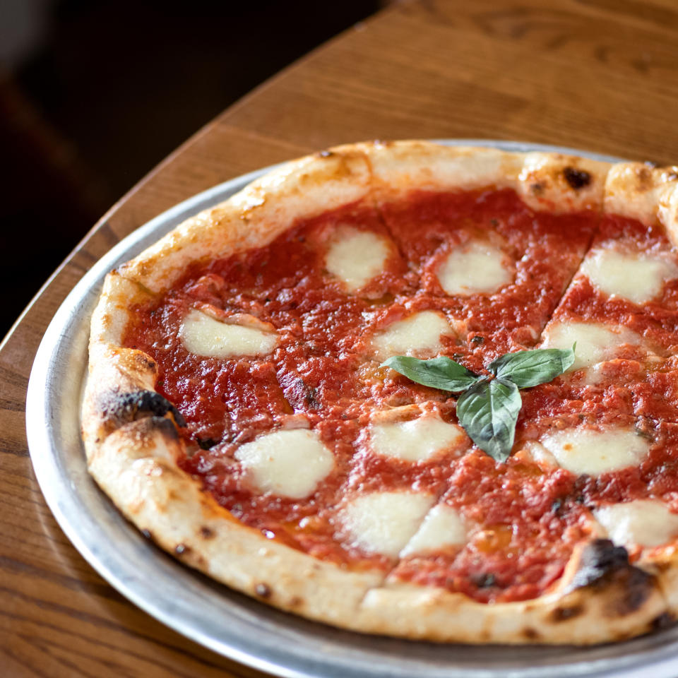 Whole pizza with tomato sauce and cheese, garnished with basil on a tray