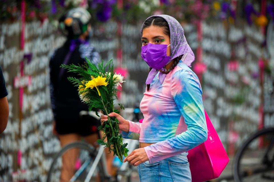 Woman by metal fence with the names of victims of femicide in Mexico City on the eve of International Women's DayAFP via Getty Images