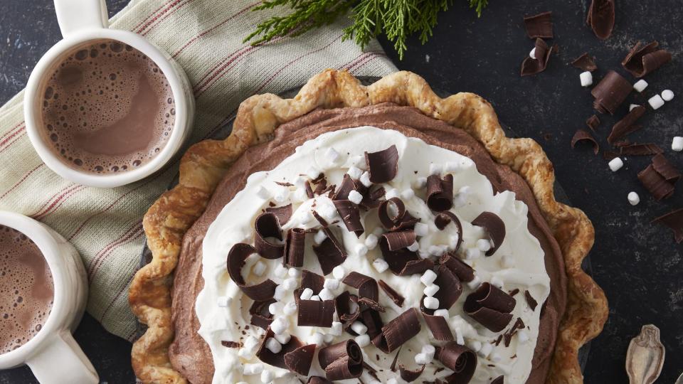 hot chocolate ice box pie in a metal pie plate with two mugs of hot cocoa and a pie server next to it